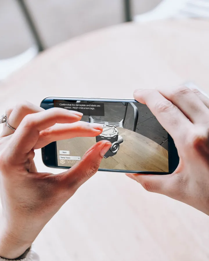 Manos sosteniendo un celular con una escena de realidad aumentada