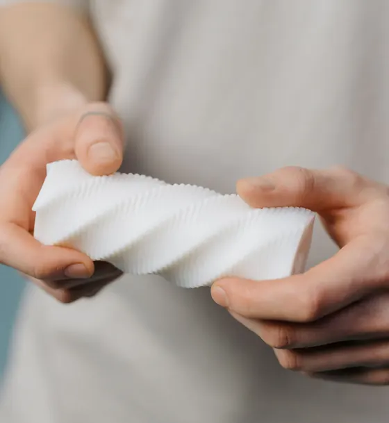 Manos sosteniendo una pieza blanca con relieve en espiral impresa en 3D