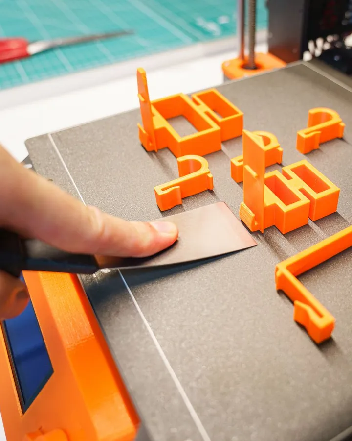 Piezas naranjas recién impresas en 3D sobre la cama de una impresora